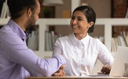 A man and a woman sitting at a desk in front of a laptop computer, smiling and shaking hands. A man and a woman sitting at a desk in front of a laptop computer, smiling and shaking hands.