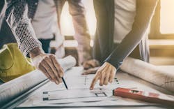A Man And Woman Review Blueprints A Hard Hat And Construction Level Sit On The Table Nearby A Man And Woman Review Blueprints A Hard Hat And Construction Level Sit On The Table Nearby