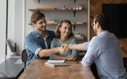A Smiling Man And Woman Sit At A Table Across From Another Man The Two Men Are Shaking Hands Over The Table A Smiling Man And Woman Sit At A Table Across From Another Man The Two Men Are Shaking Hands Over The Table