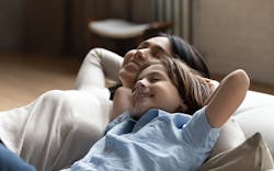 A Woman And A Child Are Resting Comfortably Together On A Couch, Smiling, With Their Hands Behind Their Heads A Woman And A Child Are Resting Comfortably Together On A Couch, Smiling, With Their Hands Behind Their Heads