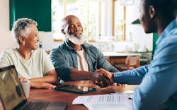 Two homeowners sit across their kitchen table from a contractor. One of the homeowners is shaking the contractor’s hand. Two homeowners sit across their kitchen table from a contractor. One of the homeowners is shaking the contractor’s hand.