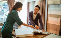 Two people review a large sample book together on a table in a home interior design showroom. Two people review a large sample book together on a table in a home interior design showroom.